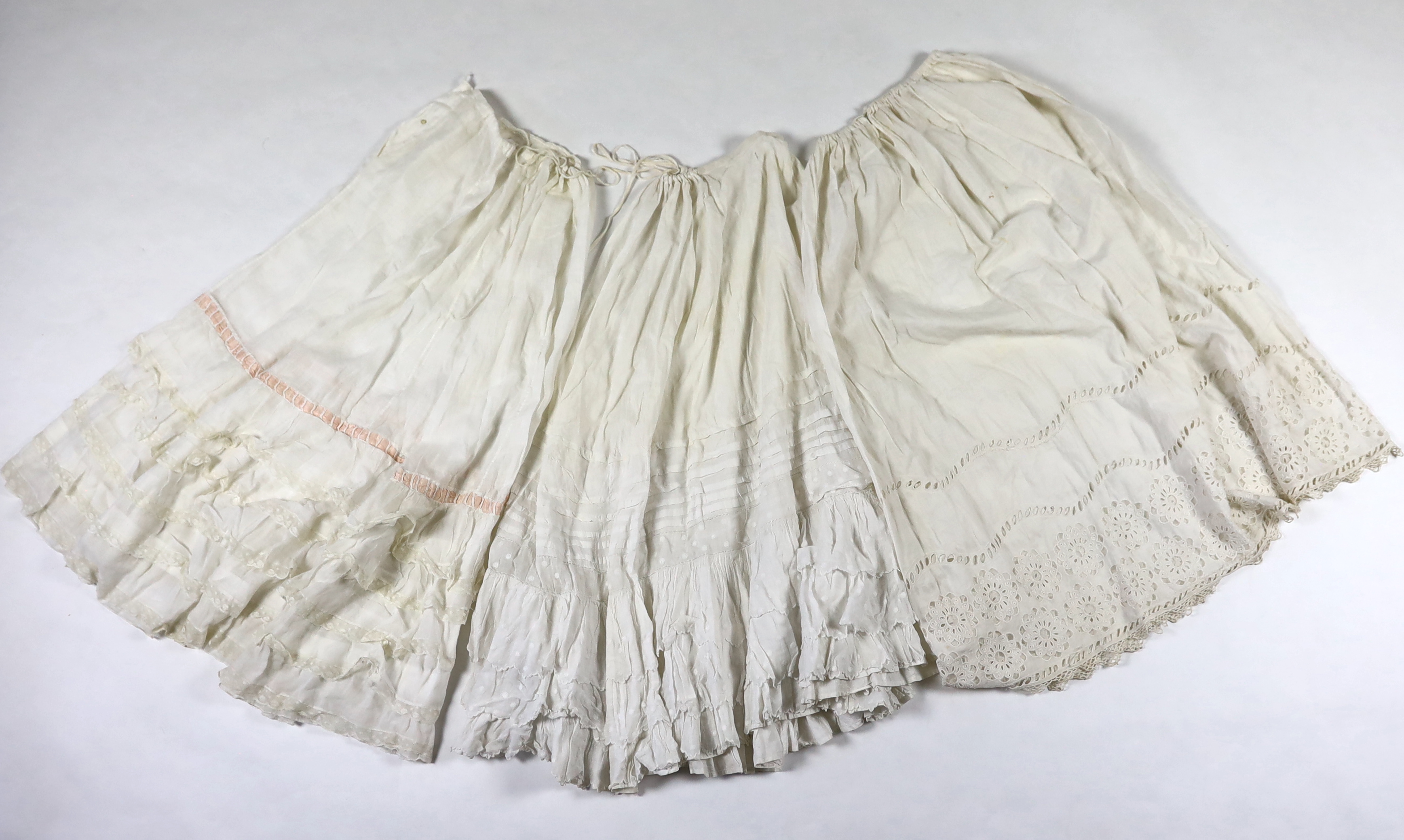 Three Victorian white worked petticoats; one two tiered, one lace trimmed with ribboning, the third worked with cutwork border, all approx. 94cm long